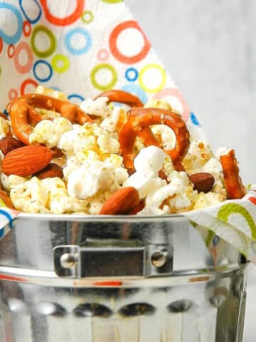 Popcorn snack mix in metal bucket with colorful napkin.