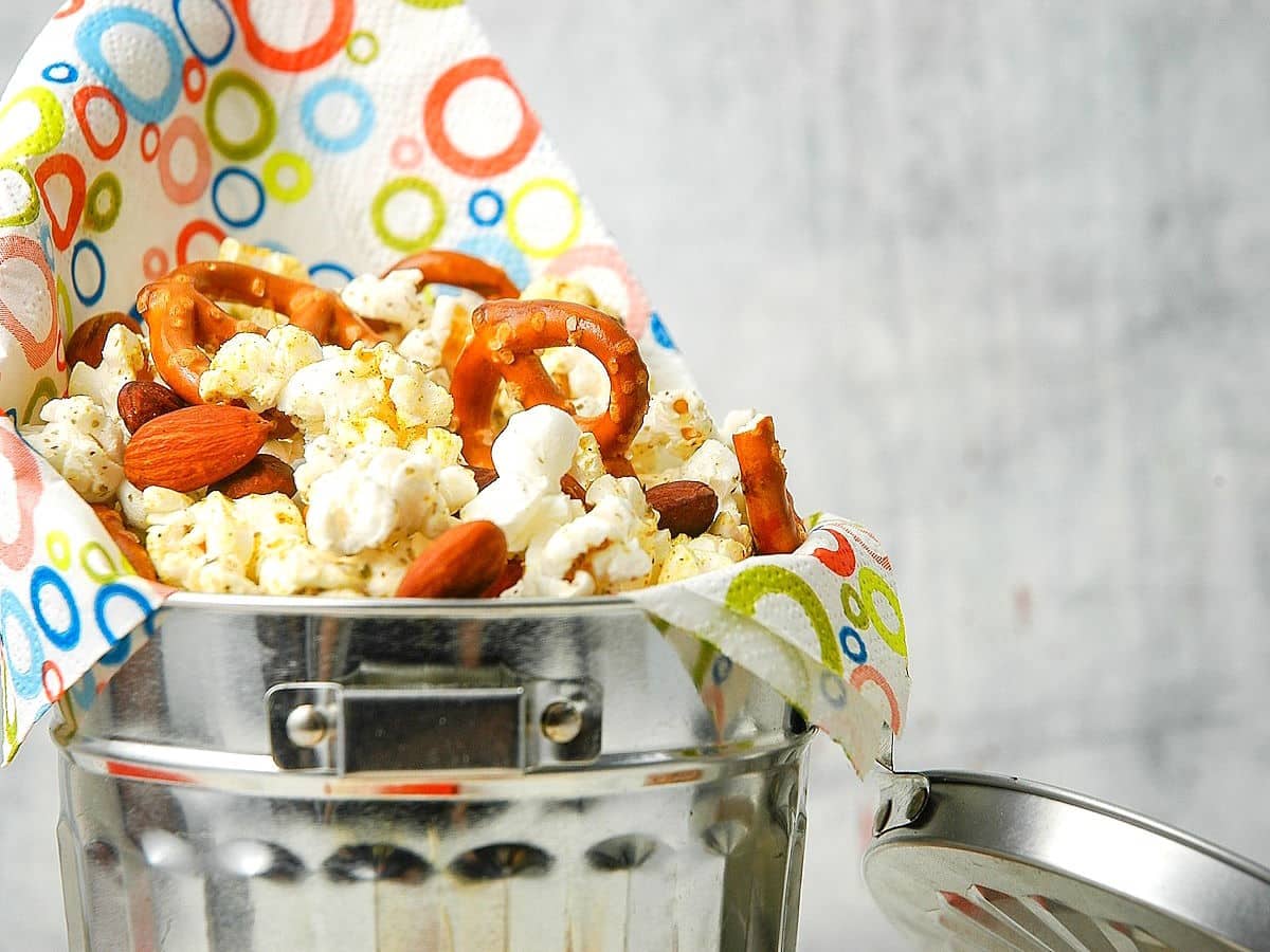 Popcorn snack mix with nuts and almonds in metal bucket.
