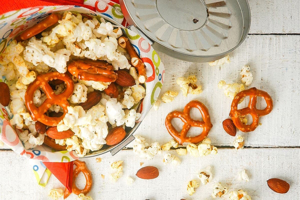 Popcorn snack mix in metal bucket on white wooden background.