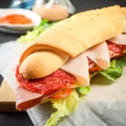 Triple meat sub sandwich on parchment lined cutting board.