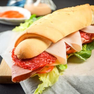 Triple meat sub sandwich on parchment lined cutting board.