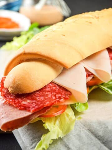Triple meat sub sandwich on parchment lined cutting board.