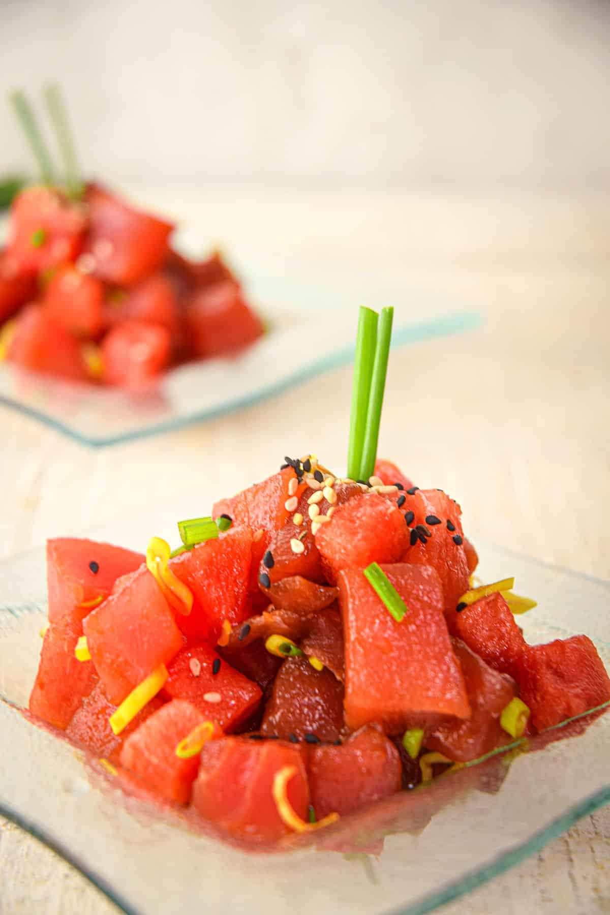 Tuna watermelon tartare on a clear glass plate with chives and sesame seeds.
