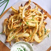 Golden turnip fries on parchment lined serving board with dip.