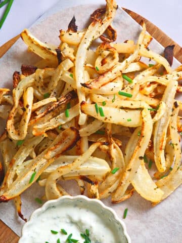 Golden turnip fries on parchment lined serving board with dip.