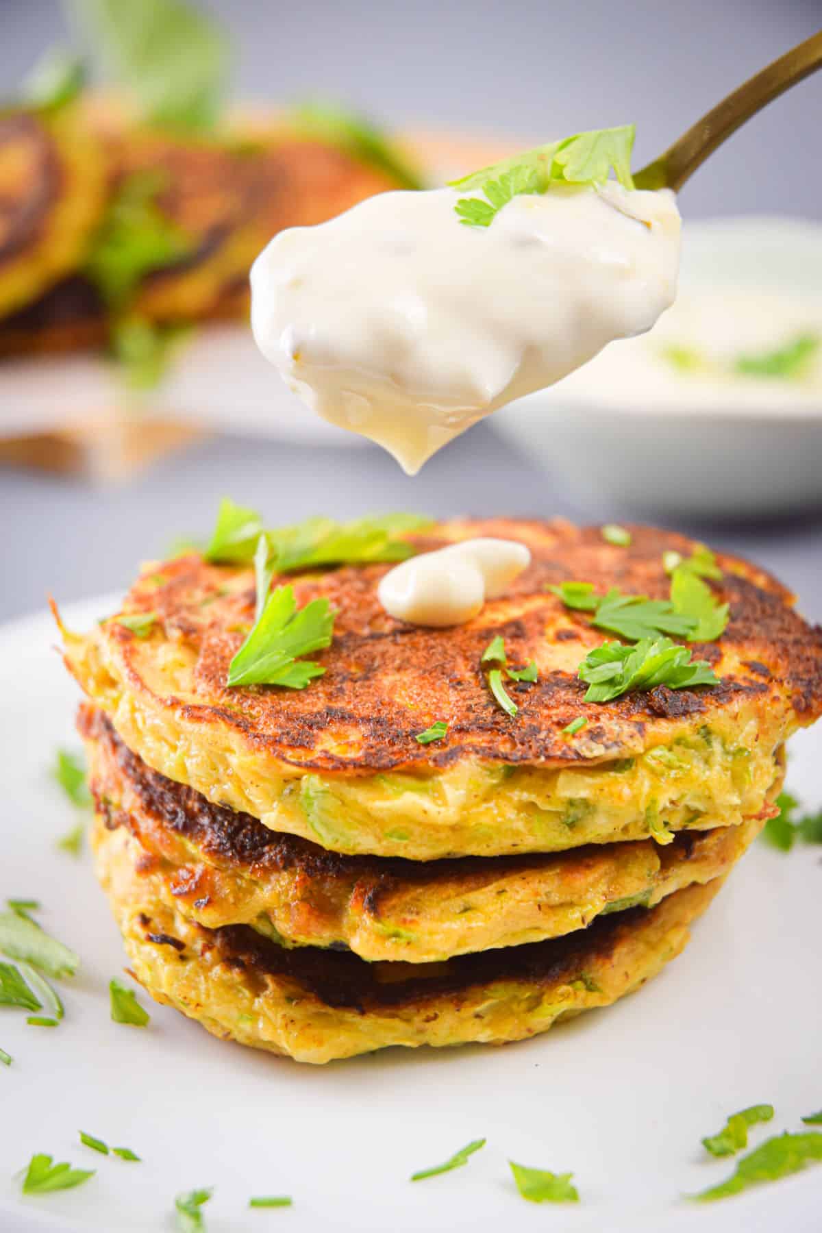 Vegetarian zucchini crab cakes stacked on top of each other on a plate with a spoon of tartar sauce.