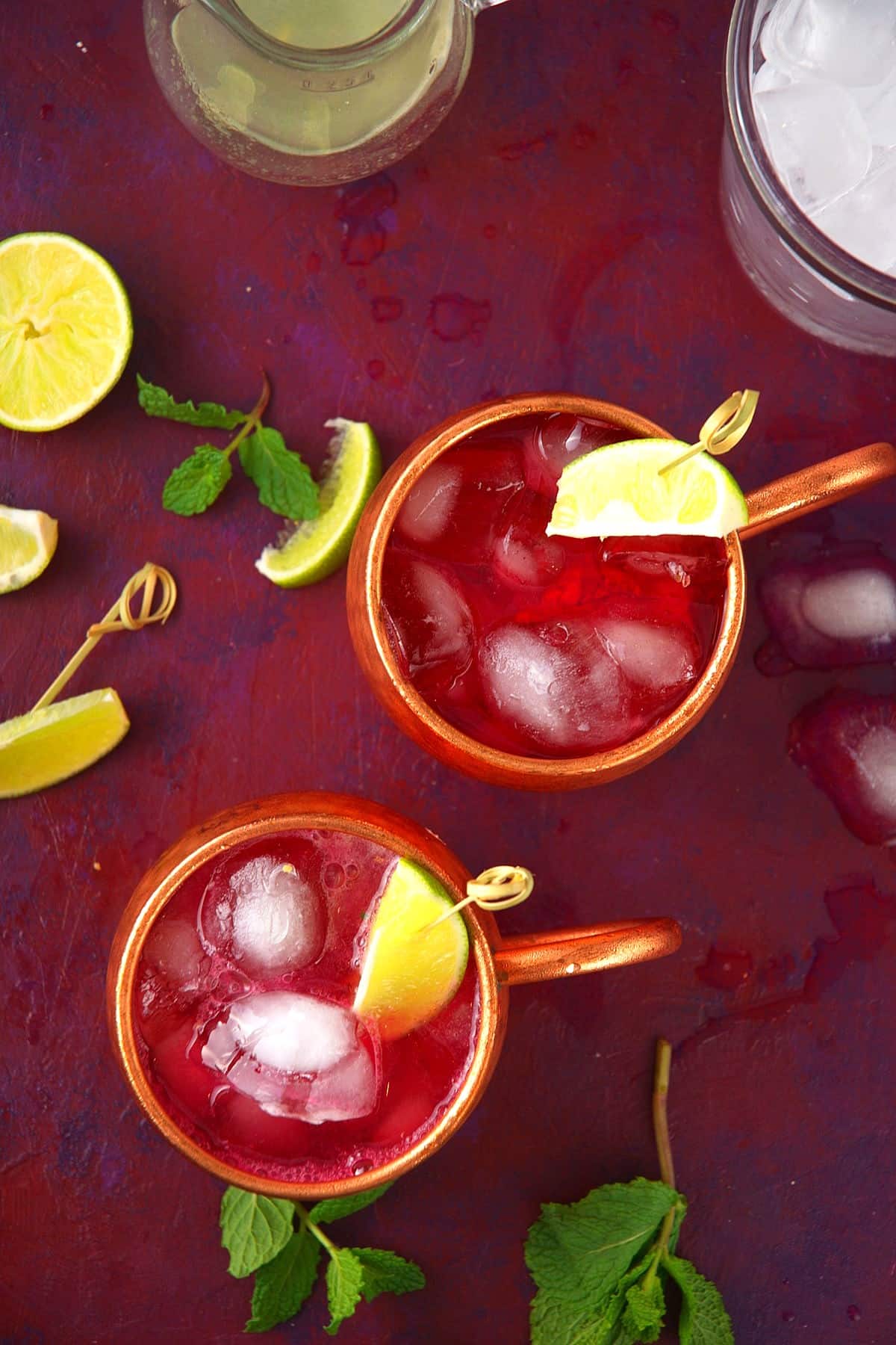 Virgin Moscow mules in copper glasses with lime wedge garnishes on burgundy background.