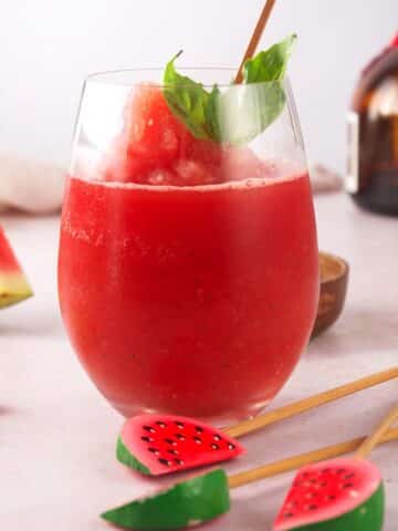 Watermelon basil cocktail in wine glass with watermelon swizzle stick.