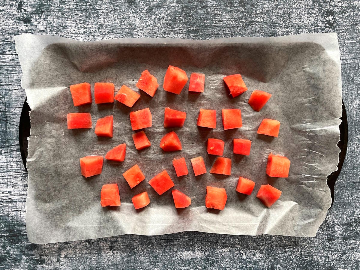 Watermelon cubes on wax paper lined sheet pan.