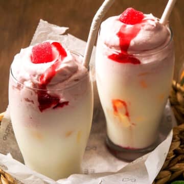 Whipped strawberry milk in 2 glasses with paper straws.