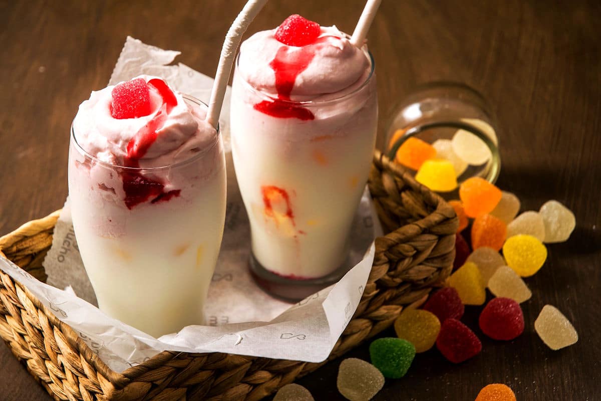 Whipped strawberry milk in 2 glasses with paper straws and jelly candies on the side.