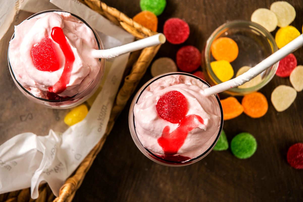 Whipped strawberry milk in 2 glasses with paper straws and jelly candies.