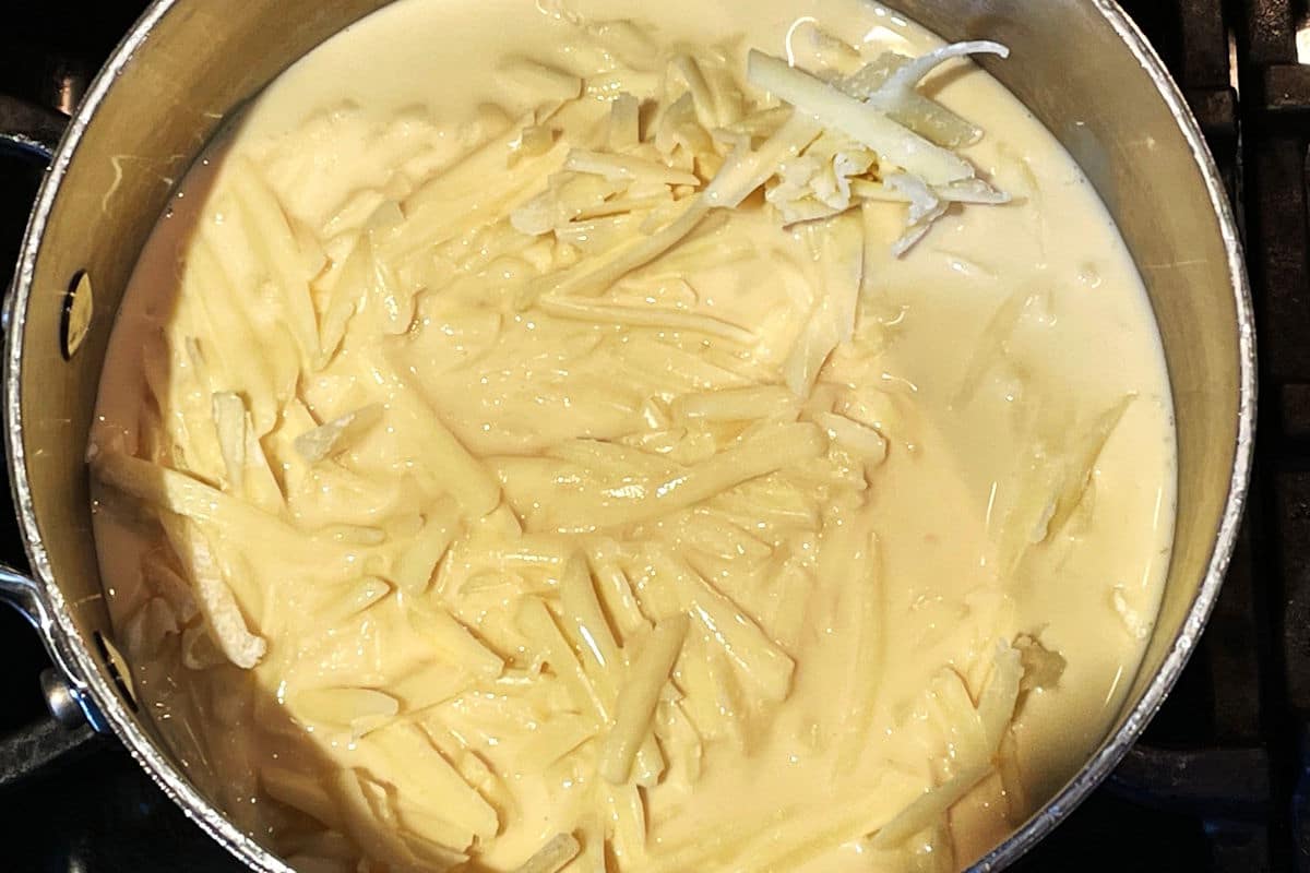 Shredded white cheddar and evaporated milk in saucepan.