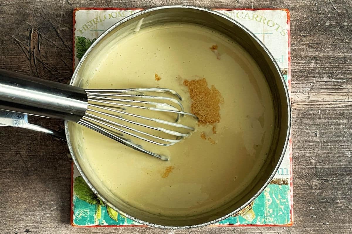 White nacho cheese sauce in saucepan with whisk.